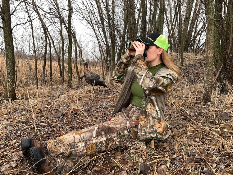 Woman looking through binoculars sitting while turkey hunting