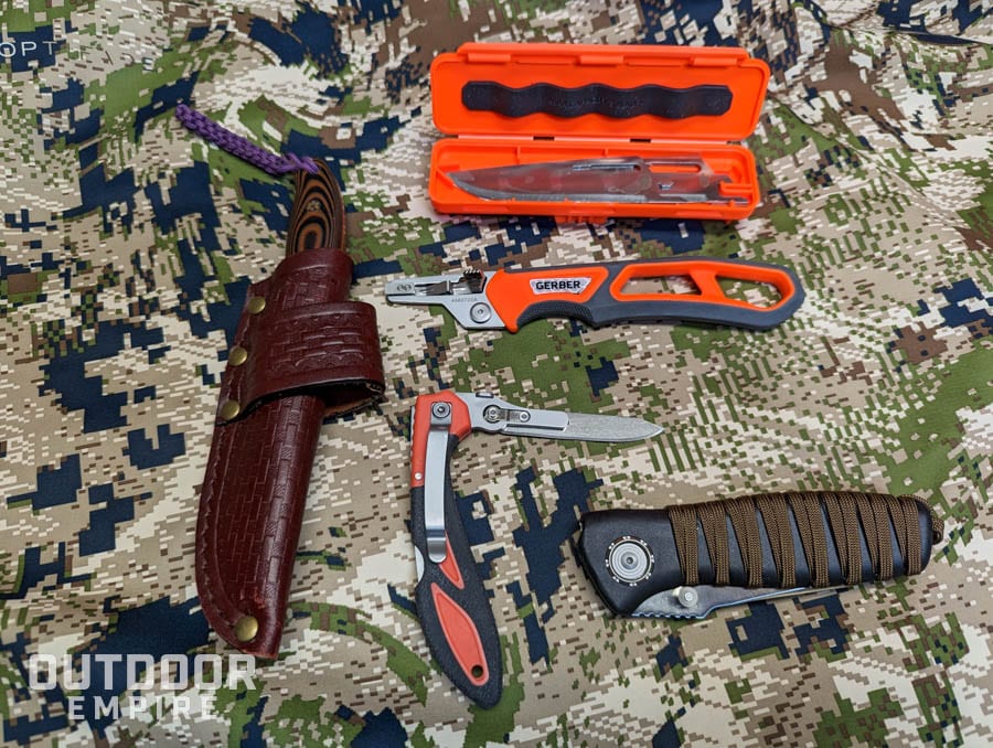 Four different types of hunting knives laid out on a camouflage fabric