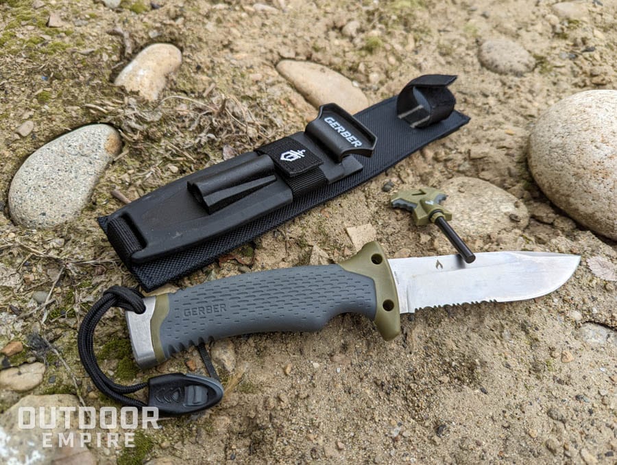 A gerber survival knife laying on dirt with sheath and ferro rod