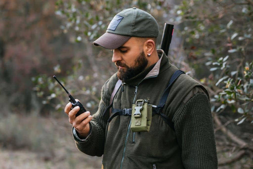 A hunter holding a walkie talkie in hand and looking at it