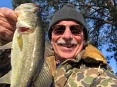 Man with coat and beanie on holding bass fish caught in winter