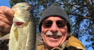 Man with coat and beanie on holding bass fish caught in winter