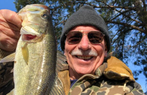 Man with coat and beanie on holding bass fish caught in winter