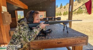Man in hunting camo ranging distance with rifle scope sitting at gun range bench