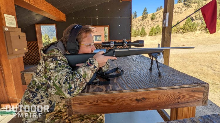 Man in hunting camo ranging distance with rifle scope sitting at gun range bench