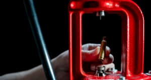 A hand inserting a 6.5 creedmoor rifle casing into a reloading press