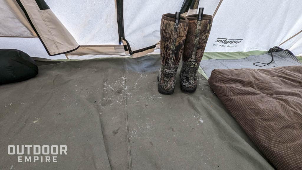 Winter boots sitting on a canvas tarp in a hot tent while camping in cold weather