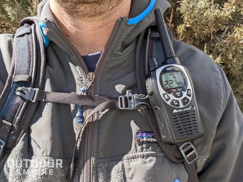 A walkie talkie attached to the backpack strap of a hiker.
