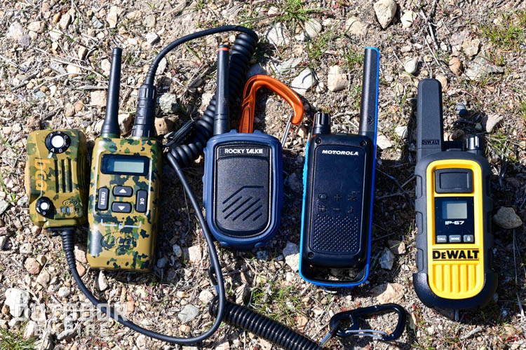 Five types of walkie talkies laying in the rocks, side by side.