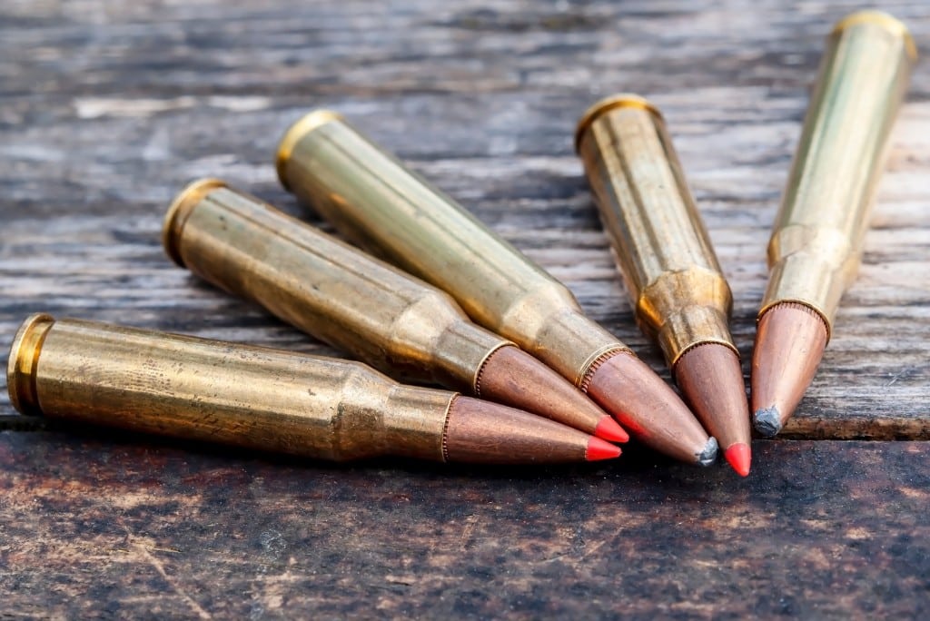 Five hunting rifle cartridges with red and silver tips sitting on a table close up
