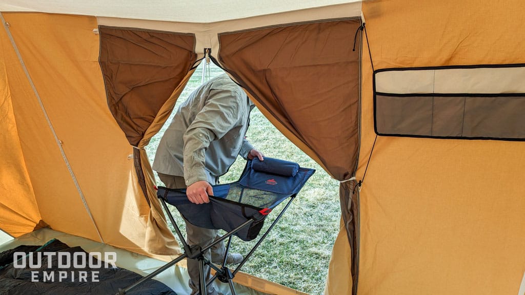 Man carrying camp chair through door of tent