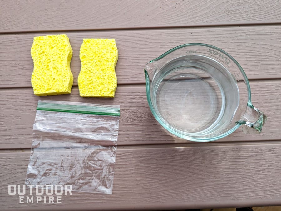 Sponges, a resealable bag, and a measuring cup of water for making a homemade ice pack on a table
