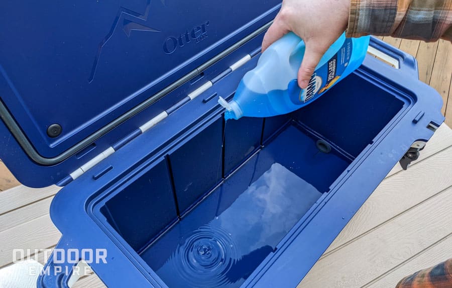 Man's hand pouring dawn dish soap into blue cooler with water for cleaning