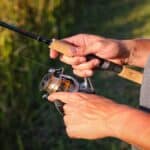 Close up of medium spinning reel size in anglers hands on a fishing rod