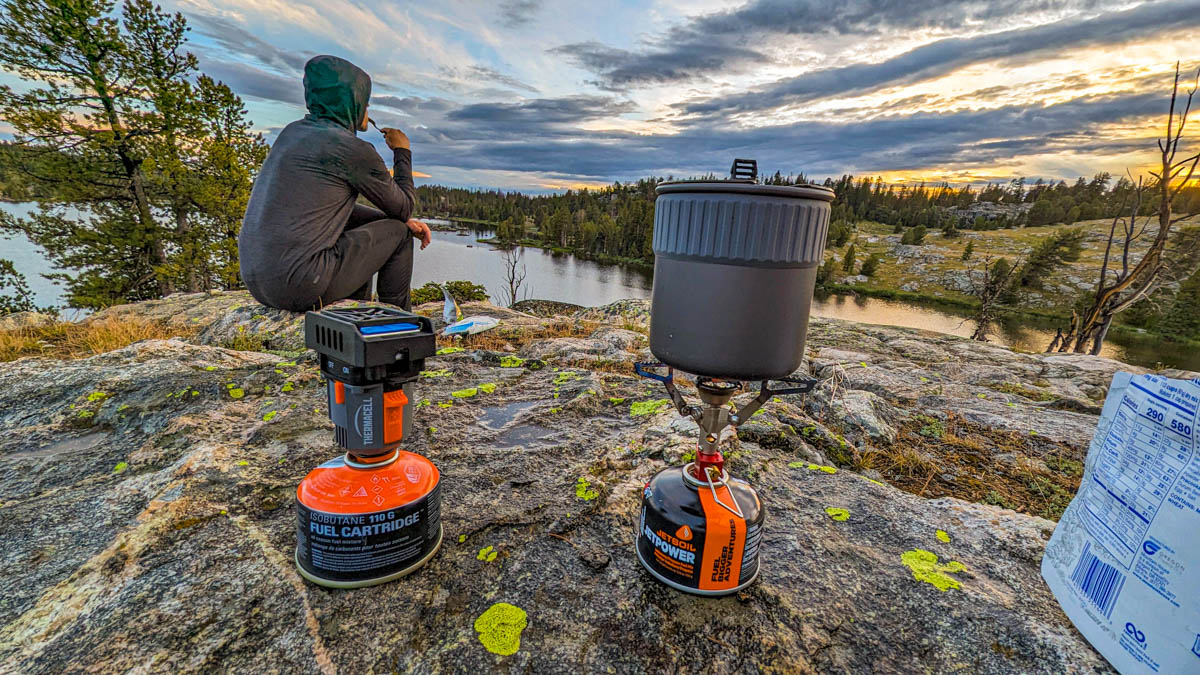 Cook stove sitting on rock with sitting man overlooking mountain lake