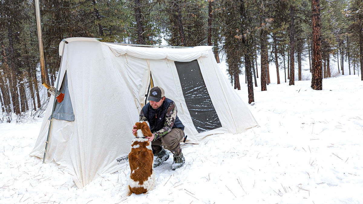 Man with dog in front of camping tent in snow