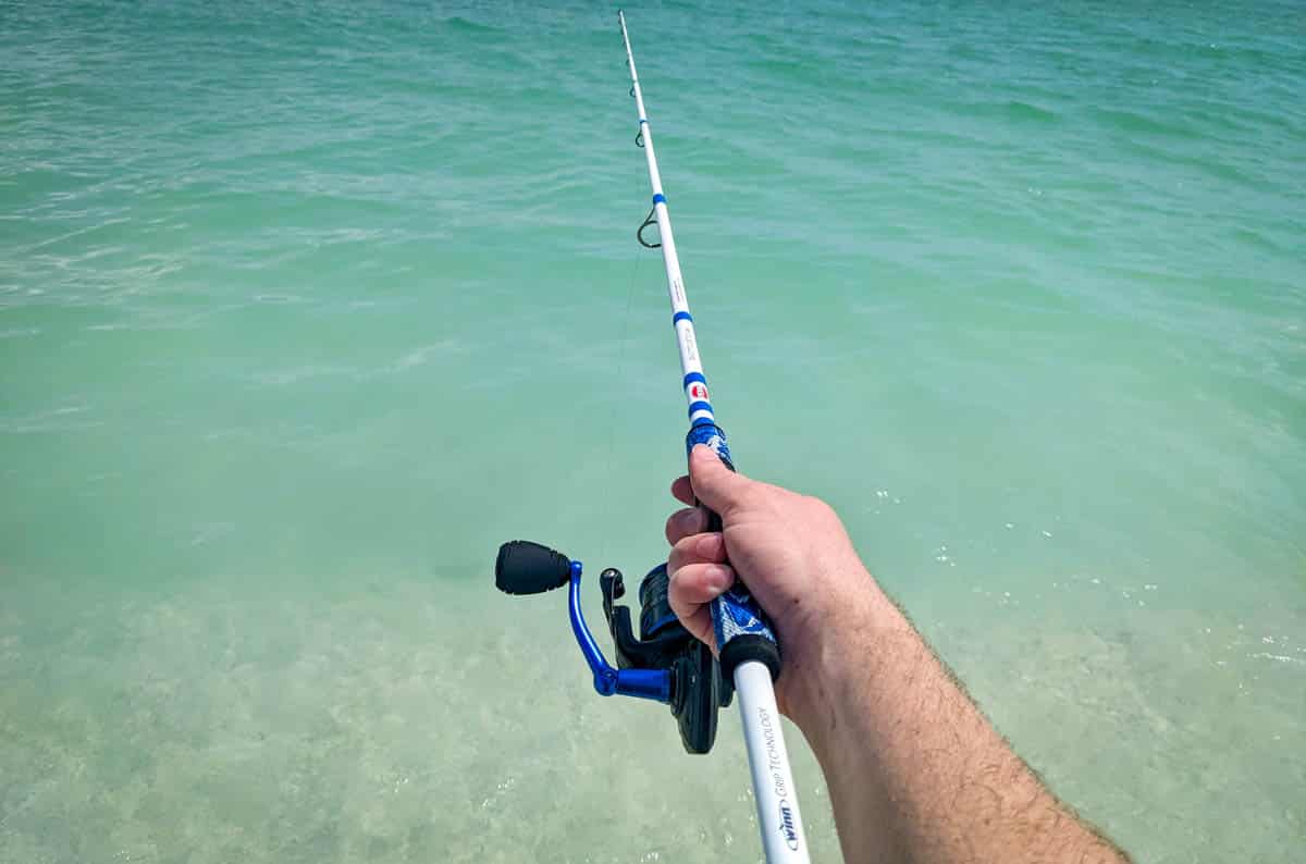 Man's hand holding fishing rod over water
